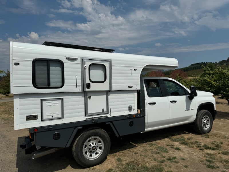 White Alaskan Flatbed Camper on a truck flatbed with a scenic background