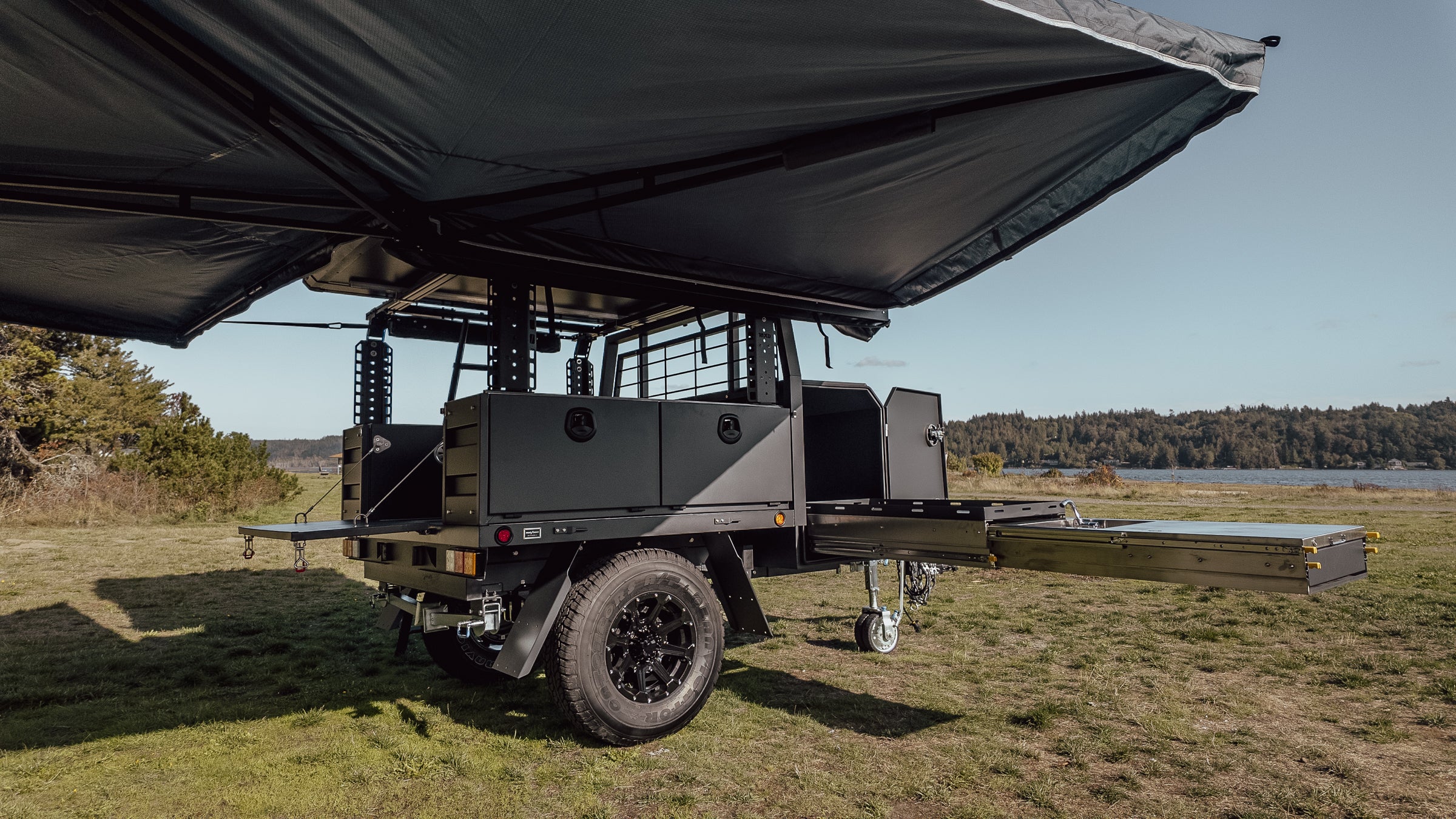 Off-road trailer with awning open and camping kitchen and tailgate on next jump outfitters trailer by a lake