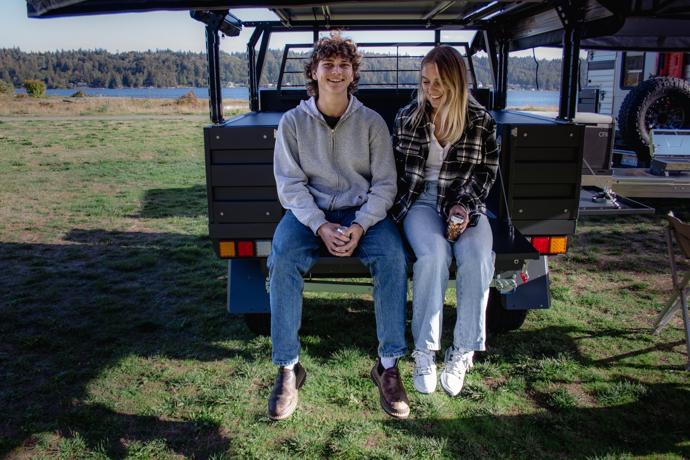 Young couple hanging out sitting on tailgate on a Next Jump Outfitters Flatbed camping by a lake