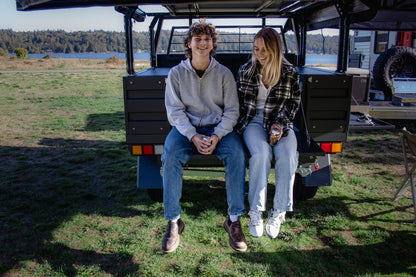 Young couple hanging out sitting on tailgate on a Next Jump Outfitters Flatbed camping by a lake